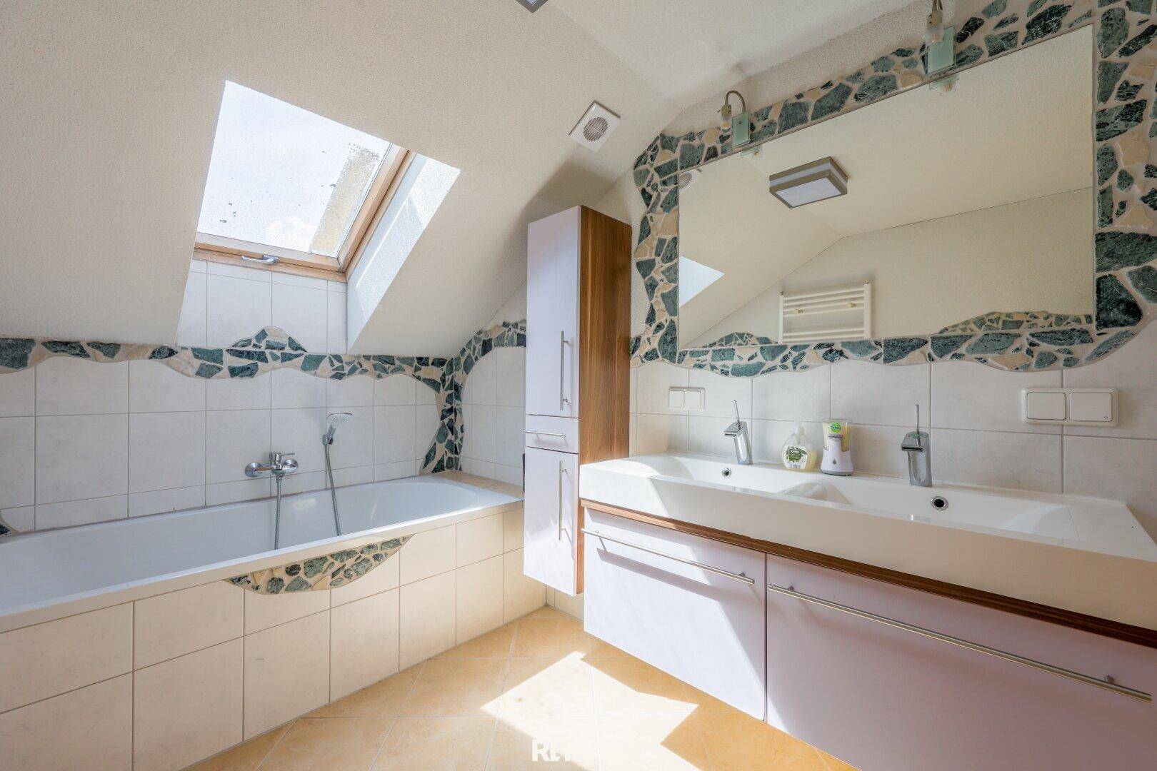Helles Badezimmer mit Badewanne, Doppelwaschbecken und Dachfenster für natürliches Licht.