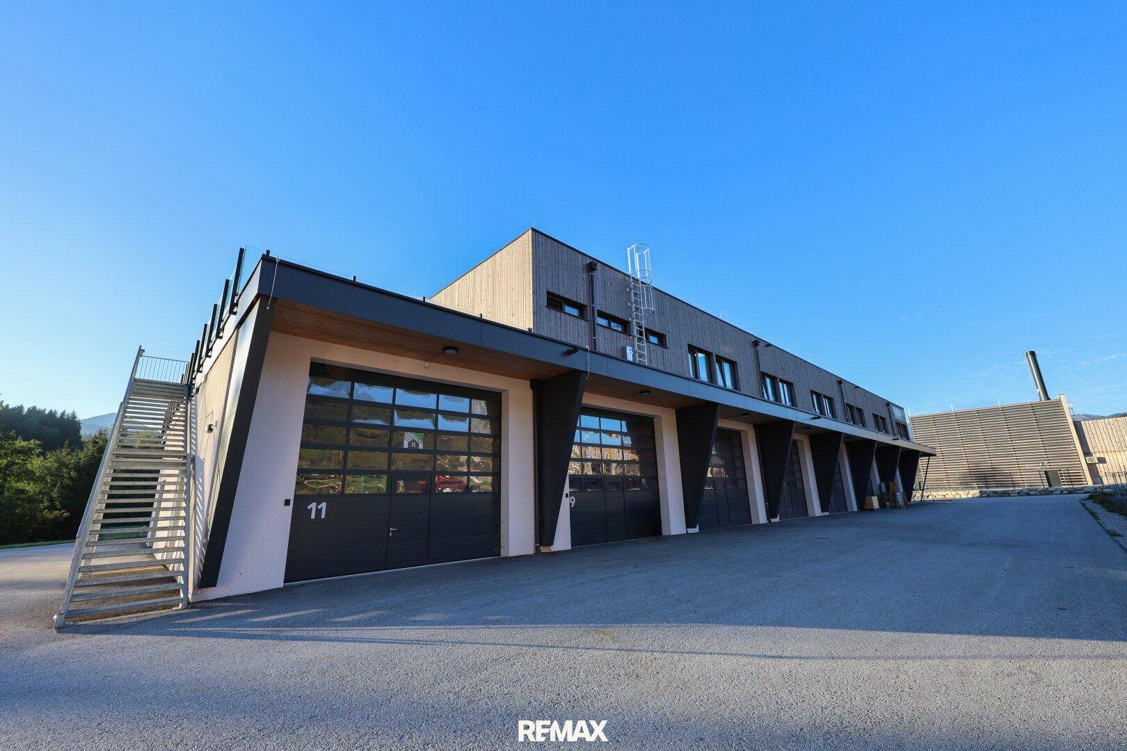 Moderne Gewerbeimmobilie mit mehreren Garagentoren und Außentreppe unter blauem Himmel.
