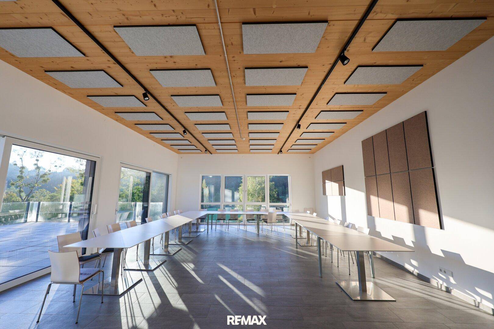 Heller Konferenzraum mit Holzbalkendecke, Schallschutzplatten und großen Fenstern mit Blick ins Grüne.