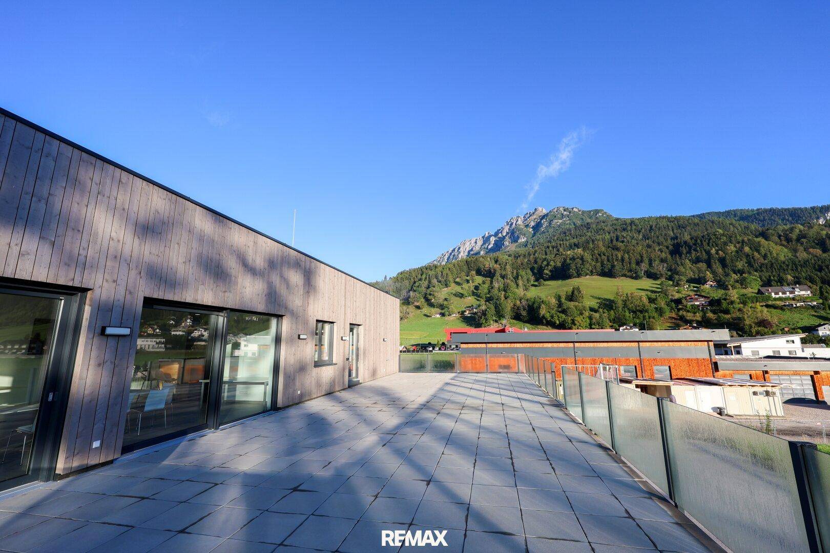 Lange Terrasse mit Glasgeländer und Panoramablick auf die umliegende Berglandschaft und das Tal.