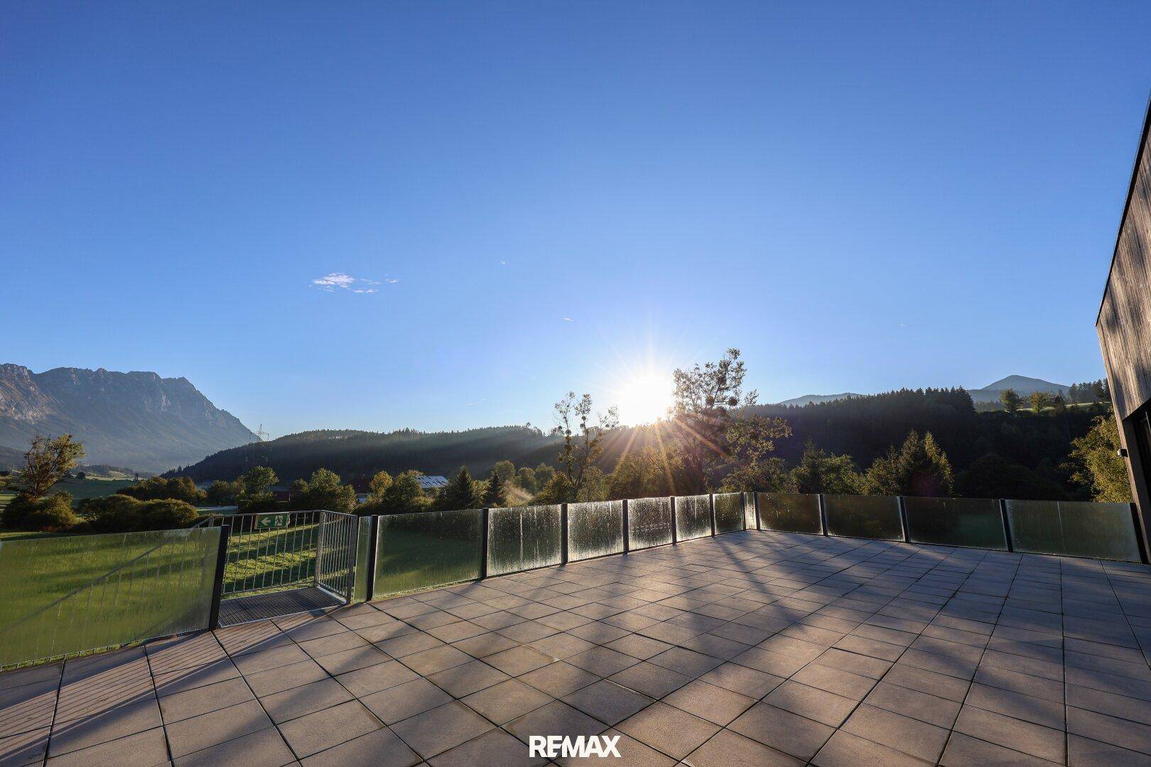 Große, gepflasterte Terrasse mit Glasgeländer und weitem Blick auf die Berge und die Landschaft.
