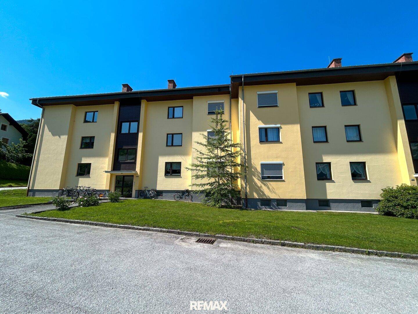 Vorderansicht eines gepflegten Mehrfamilienhauses mit gelber Fassade und grüner Rasenfläche.