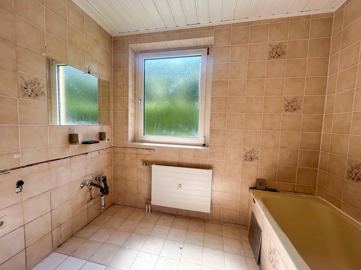 Älteres Badezimmer mit beigen Fliesen und Badewanne, benötigt eine Modernisierung.
