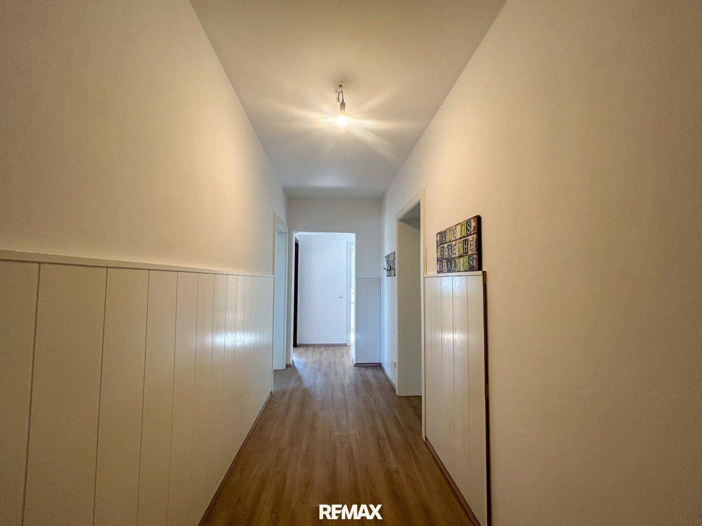 Heller Flur mit Holzoptik-Laminatboden und weißer Wandverkleidung, führt zu weiteren Räumen.
