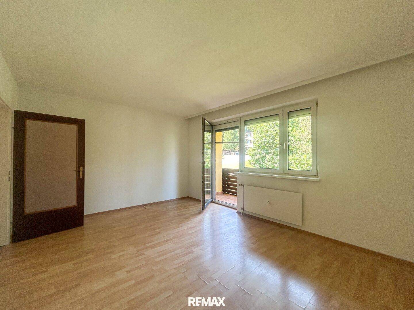 Helles Wohnzimmer mit Laminatboden und Fensterfront, die Zugang zum Außenbereich ermöglicht.
