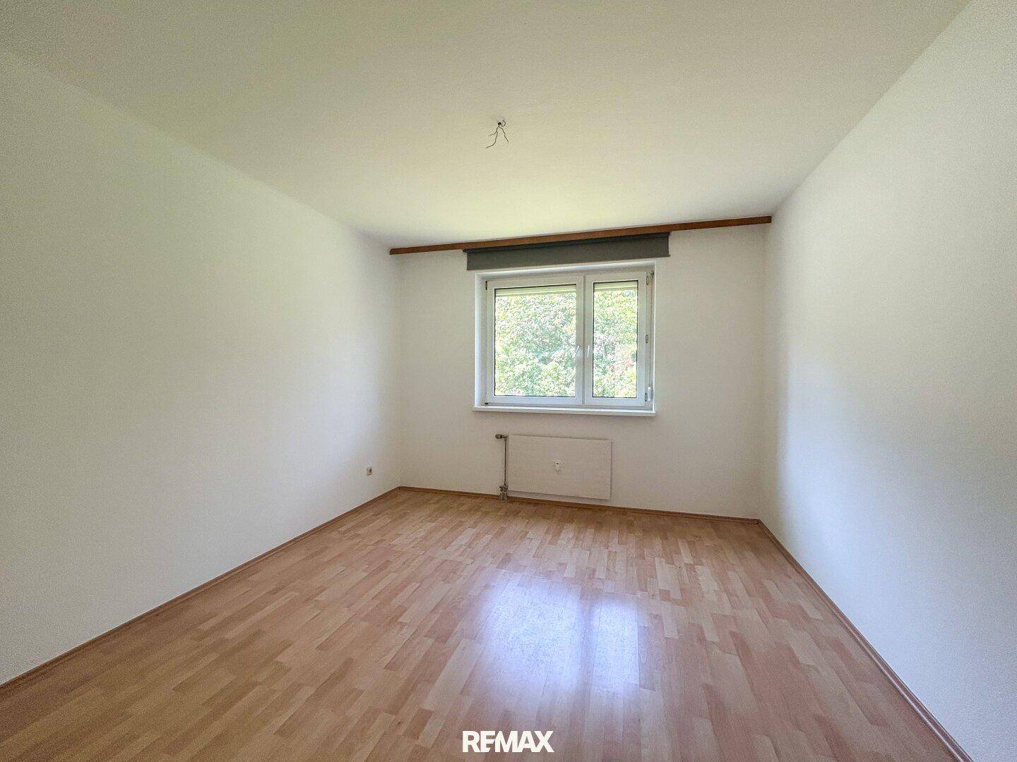 Ruhiges Schlafzimmer mit Laminatboden und einem Fenster, das eine grüne Aussicht bietet.
