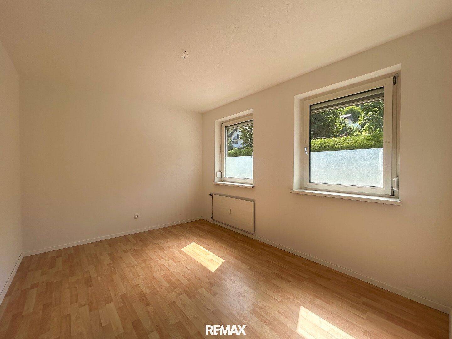 Helles Schlafzimmer mit Laminatboden und zwei Fenstern, die viel Tageslicht hereinlassen.