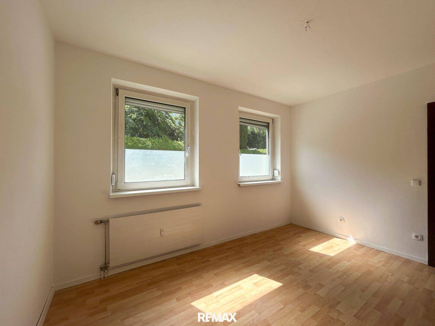 Geräumiges Schlafzimmer mit hellem Laminatboden und Fenstern mit Rollläden.