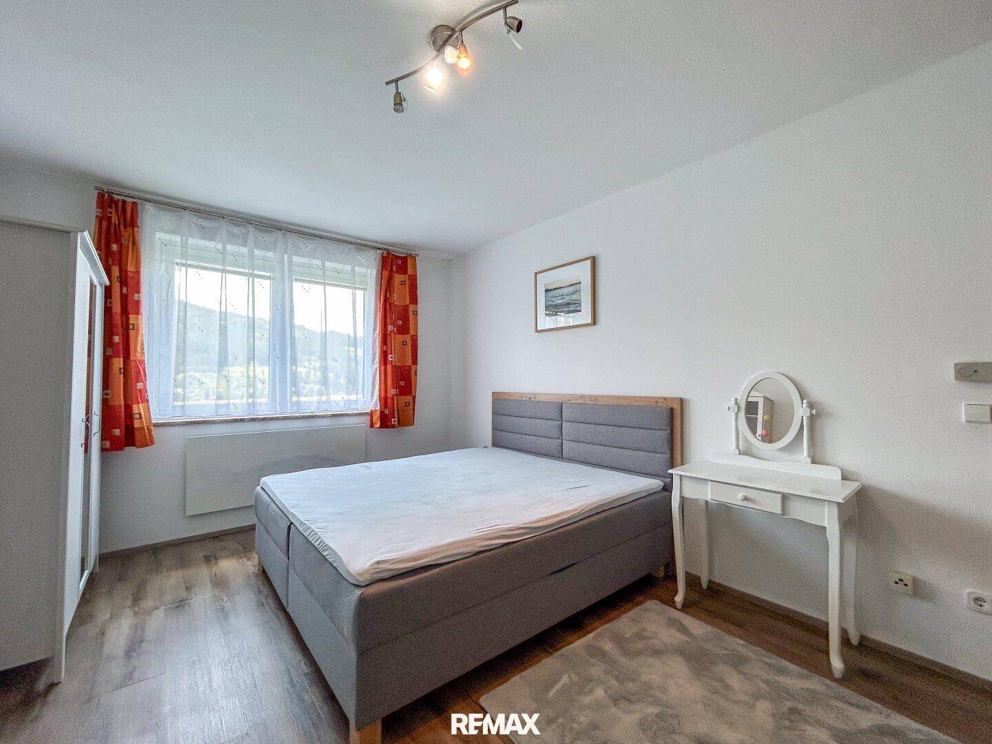 Helles Schlafzimmer mit Doppelbett, Laminatboden und Fenster mit Bergblick.