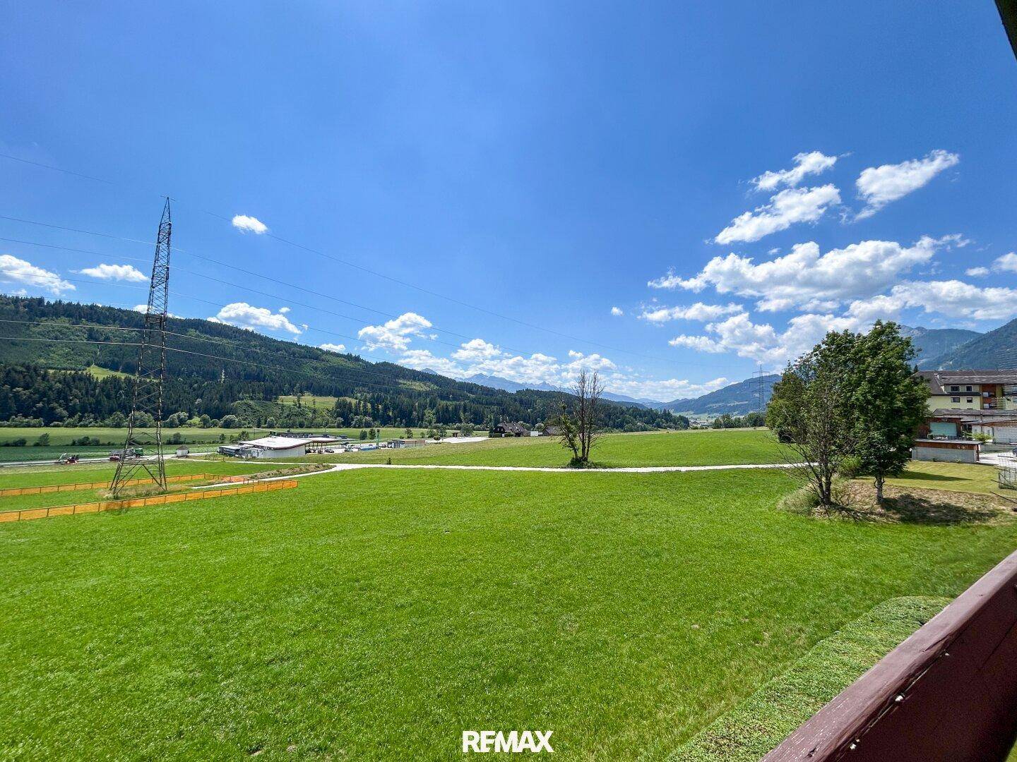 Weitläufiger Blick über grüne Wiesen, Berge und die ländliche Umgebung unter blauem Himmel.