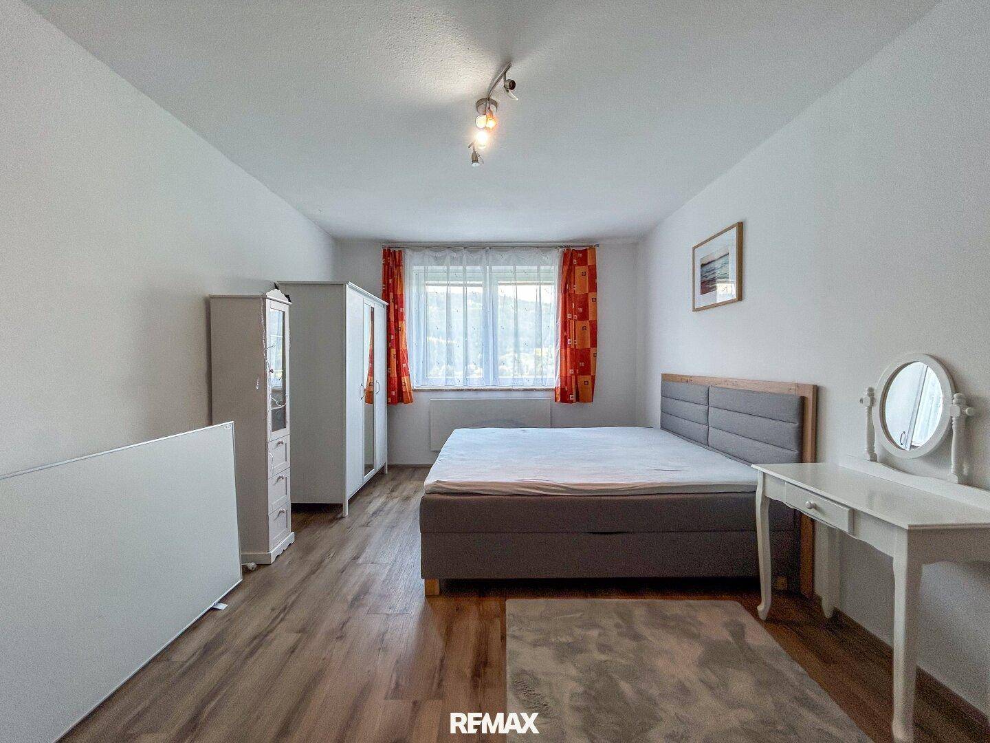 Geräumiges Schlafzimmer mit Laminatboden, weißem Kleiderschrank und Blick ins Grüne.
