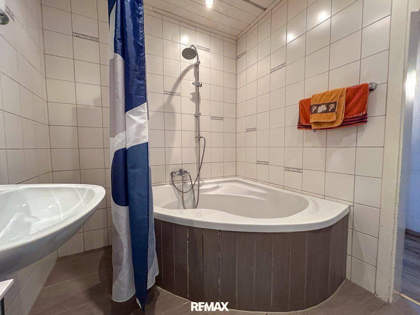 Funktionales Badezimmer mit Eckbadewanne, Duschvorhang und weißen Wandfliesen.