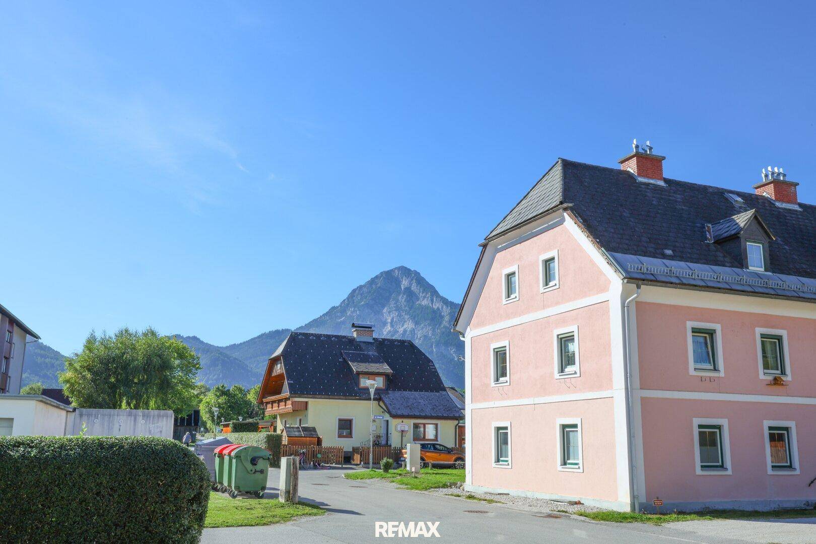 Wohngegend mit traditionellen Häusern und beeindruckendem Bergblick unter klarem, blauem Himmel.