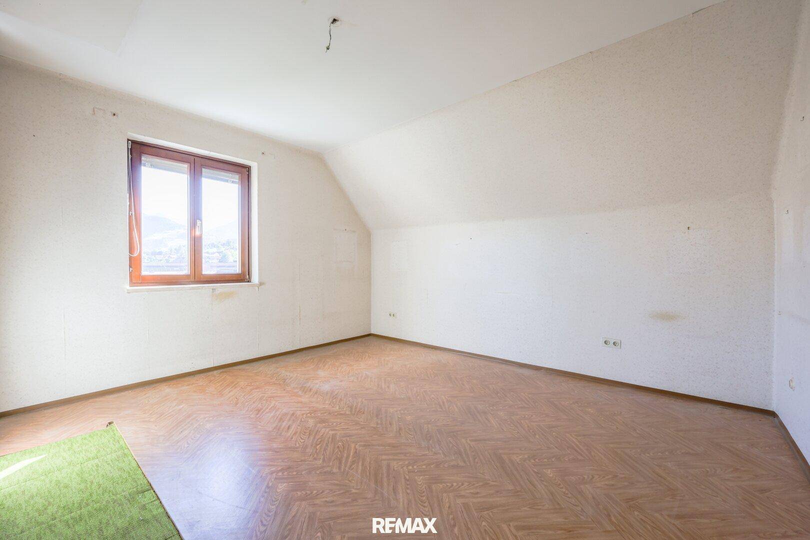 Geräumiges Schlafzimmer im Dachgeschoss mit schrägen Wänden, Laminatboden und Fenster mit Ausblick.