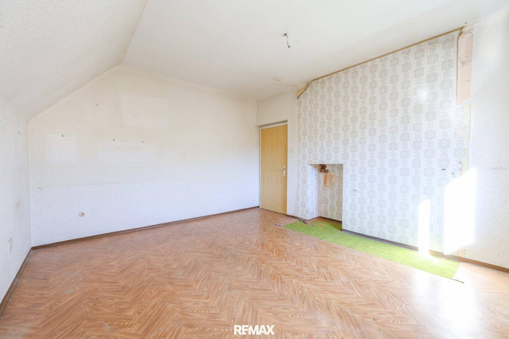 Helles Schlafzimmer im Dachgeschoss mit schrägen Wänden, Laminatboden und altem Kaminanschluss.