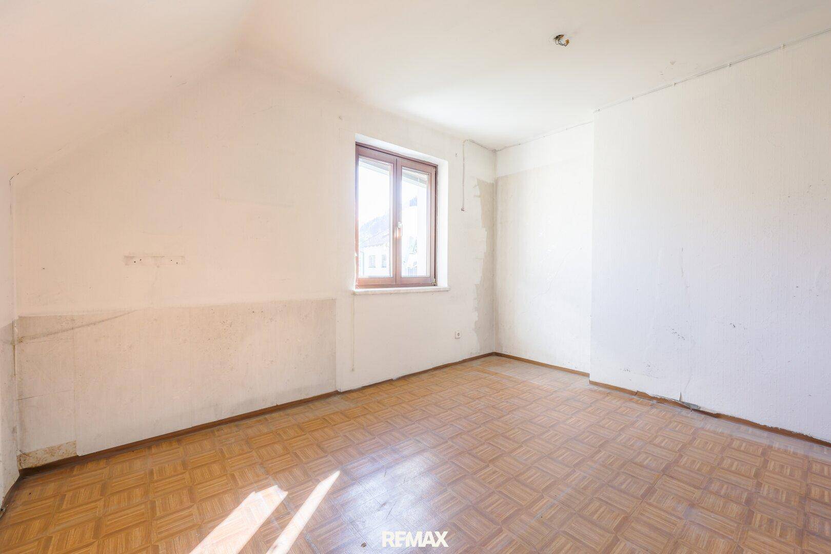 Heller Raum im Dachgeschoss mit Laminatboden, schrägen Wänden und einem Fenster für Tageslicht.