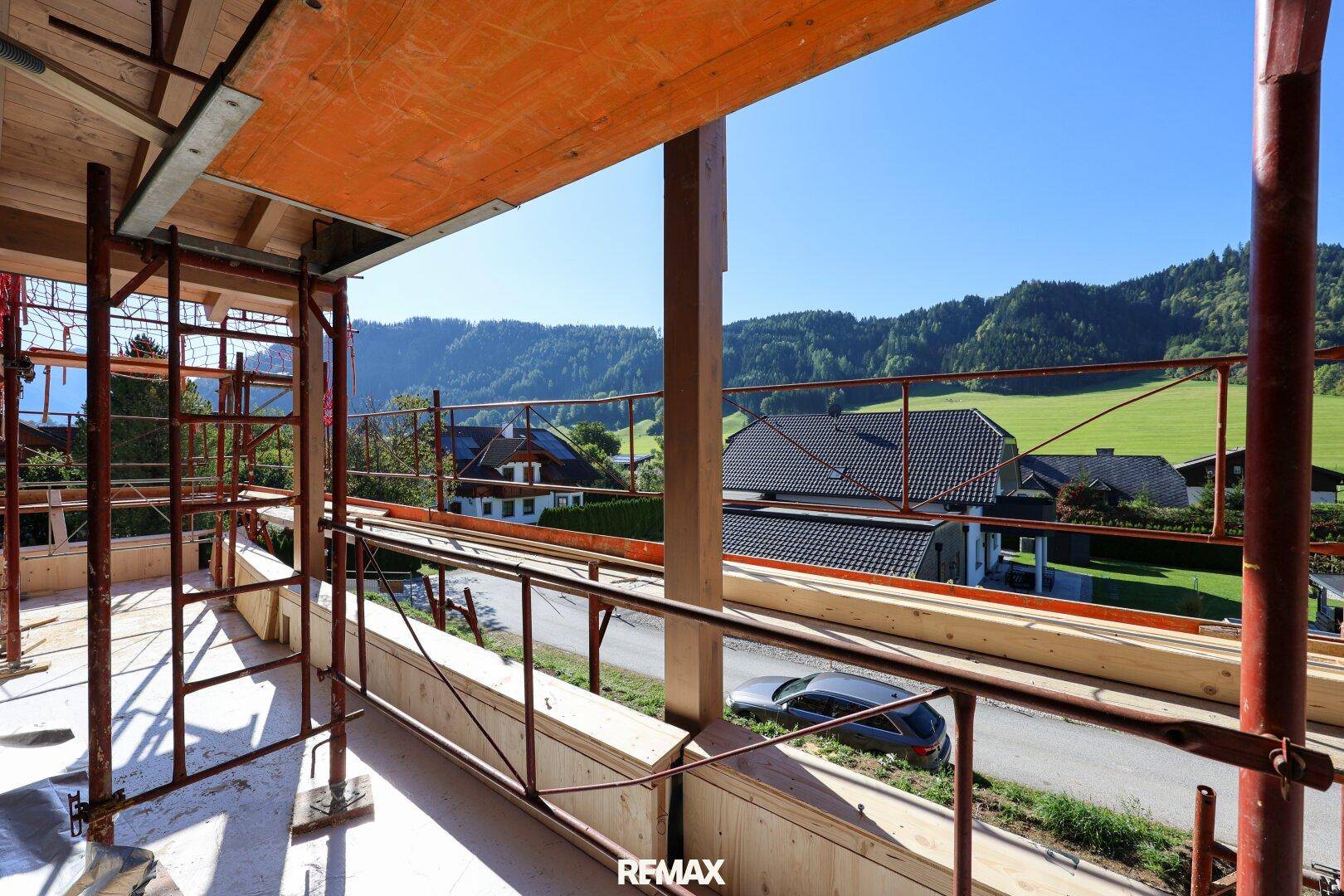 Balkon im Rohbau mit Gerüst und weitem Blick über grüne Hügel und Dächer.