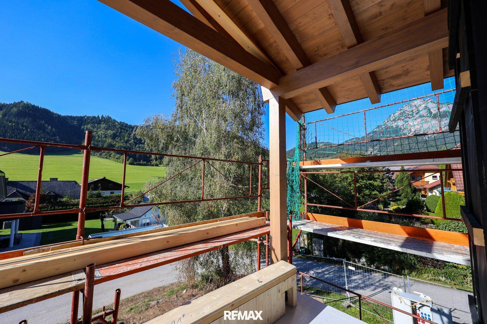 Balkon im Rohbau mit Holzkonstruktion und Blick auf grüne Landschaft und Berge.