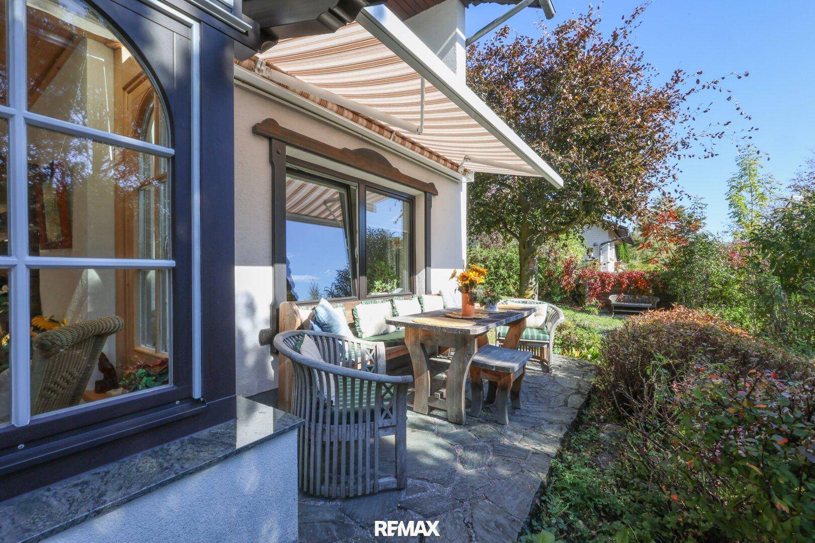 Gemütliche Terrasse mit Holztisch und Stühlen, geschützt durch eine Markise im Grünen.