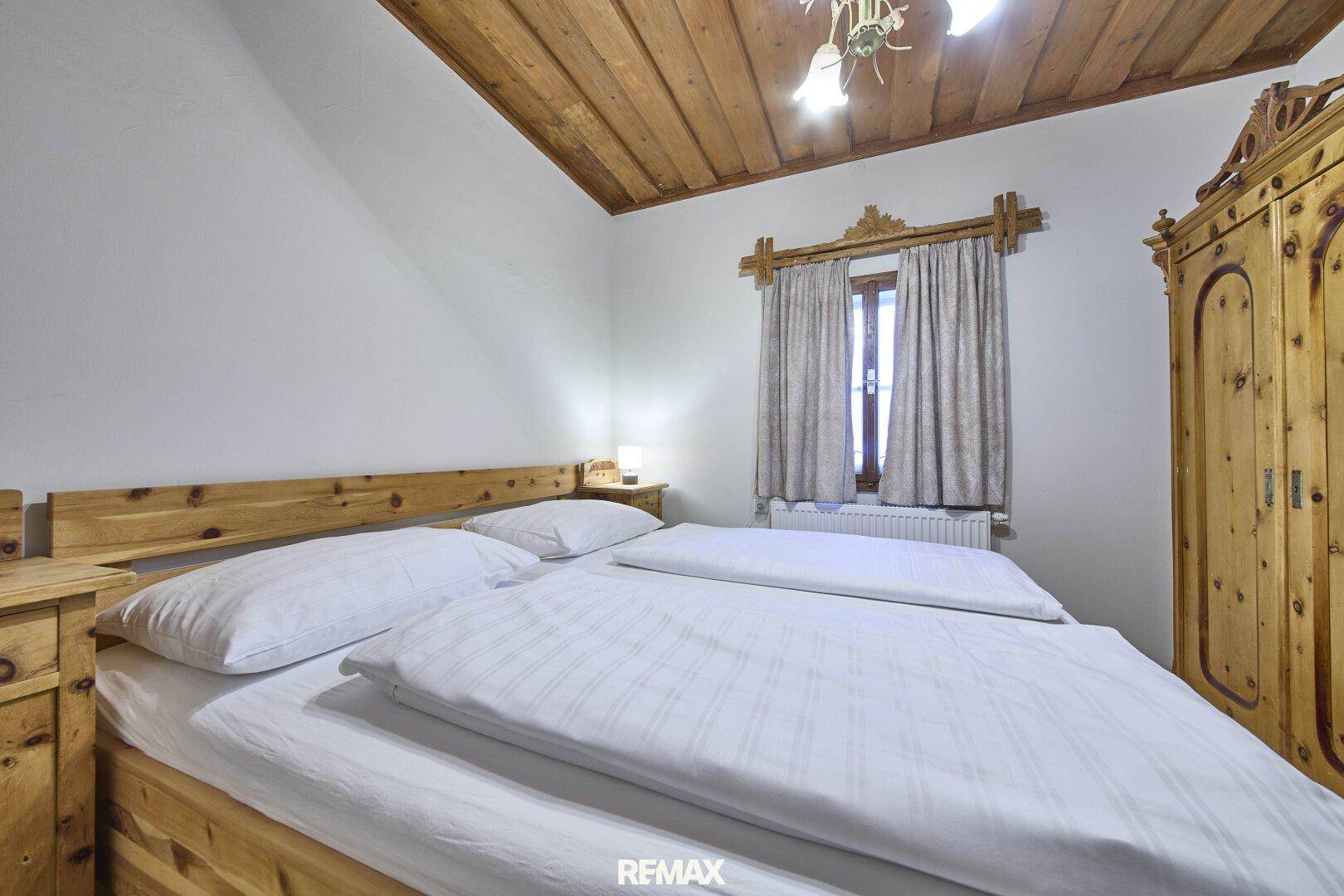 Gemütliches Schlafzimmer mit Doppelbett, Holzdecke und traditionellen Holzmöbeln im Landhausstil.