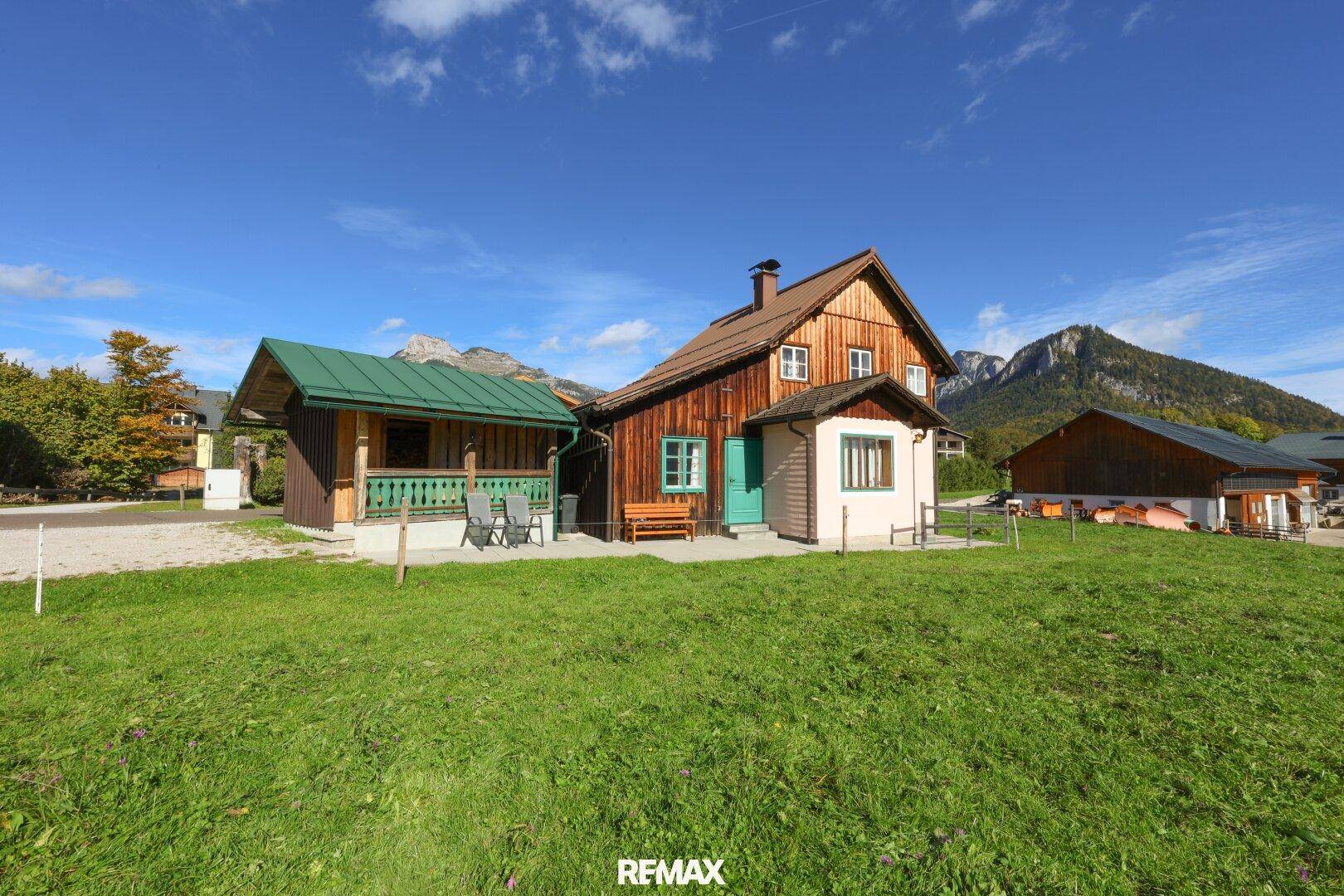 Charmantes Holzhaus mit grünem Anbau und weitläufiger Wiese in ländlicher Umgebung.