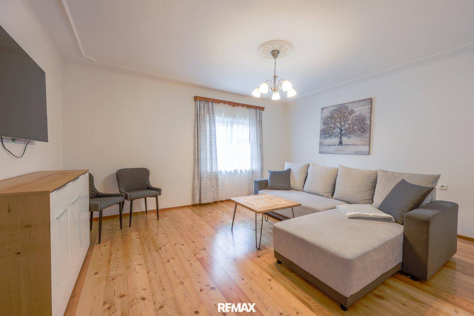 Helles Wohnzimmer mit Holzboden, gemütlichem Ecksofa und schlichter Einrichtung.