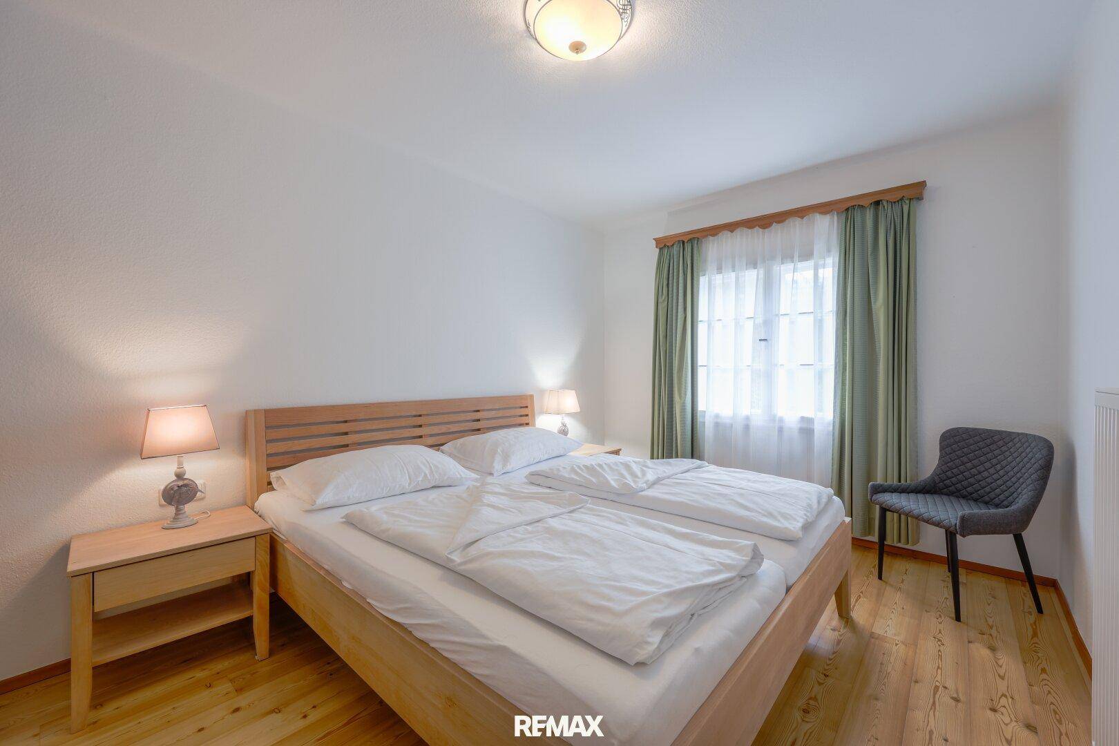 Schlichtes Schlafzimmer mit Doppelbett, Holzboden und Fenster mit Vorhängen.