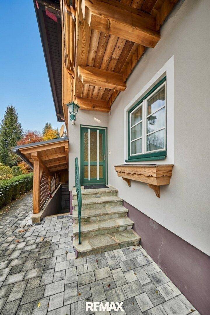 Eingangsbereich eines Holzhauses mit Steintreppe und überdachtem Zugang zum Untergeschoss.