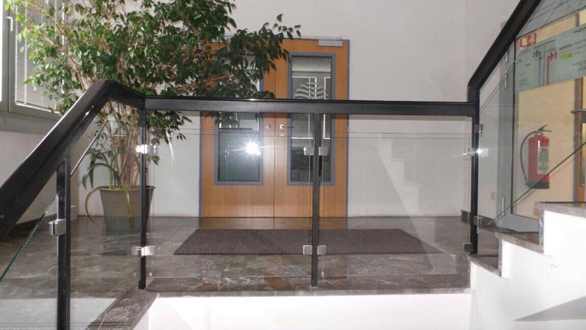 Treppenhaus mit moderner Glasbrüstung und dunklem Marmorboden, führt zu einer Holztür.