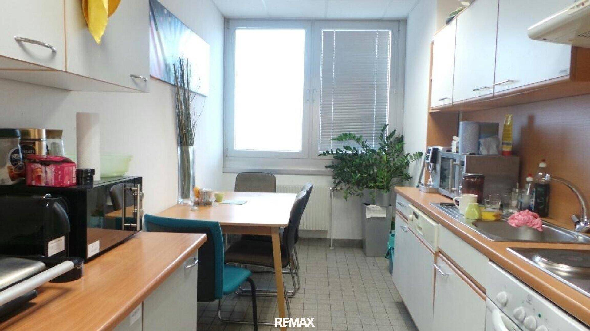 Funktionale Küche mit weißen Schränken, Holzarbeitsplatten und einem Esstisch am Fenster.
