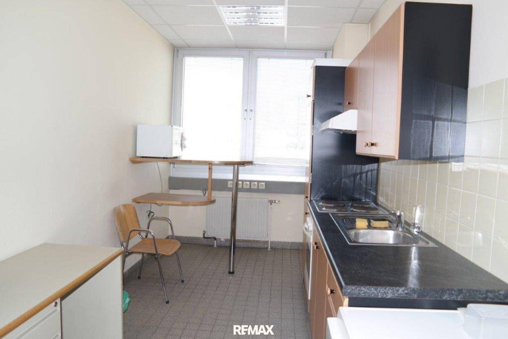 Kleine Küchenzeile mit dunkler Arbeitsplatte, hellen Holzschränken und Fensterblick.
