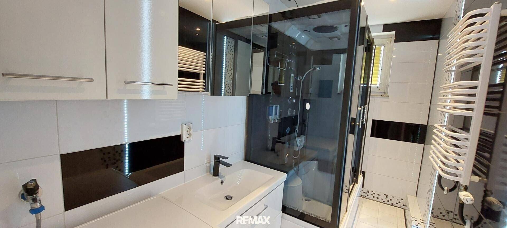 Modernes Badezimmer mit schwarz-weißen Fliesen, Einzelwaschbecken und Duschkabine.