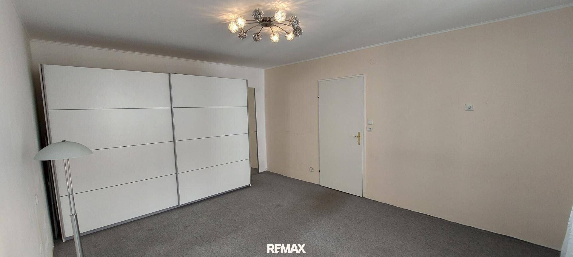 Schlafzimmer mit großem weißen Schiebetürenschrank und Teppichboden.