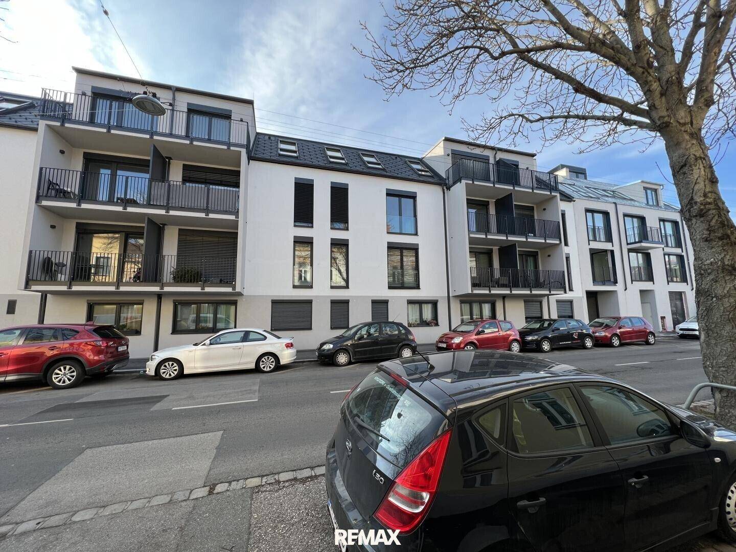 Moderne Wohngebäude mit Balkonen und großen Fenstern entlang einer städtischen Straße mit parkenden Autos.