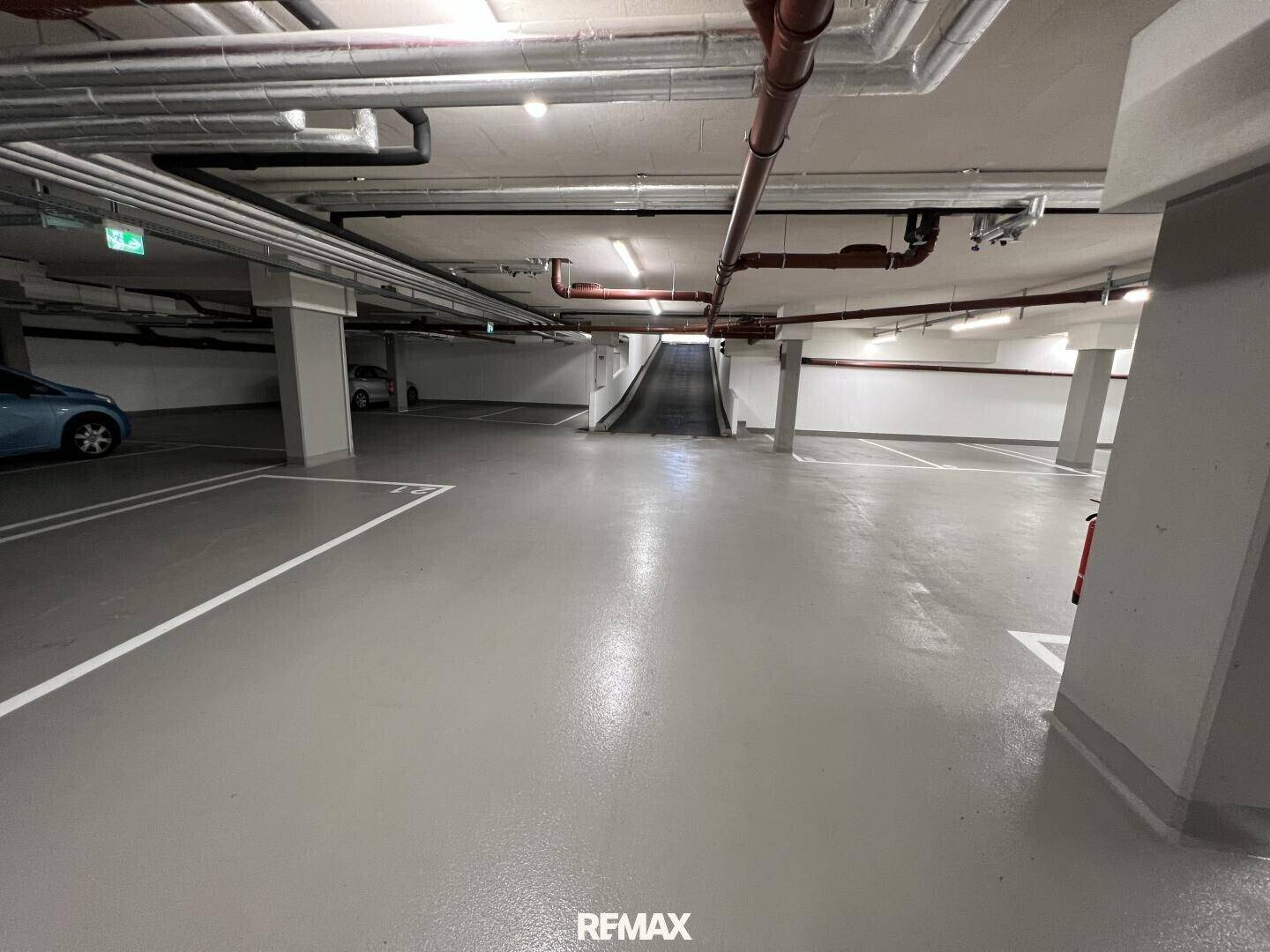 Geräumige und gut beleuchtete Tiefgarage mit markierten Parkplätzen und sichtbaren Leitungen.