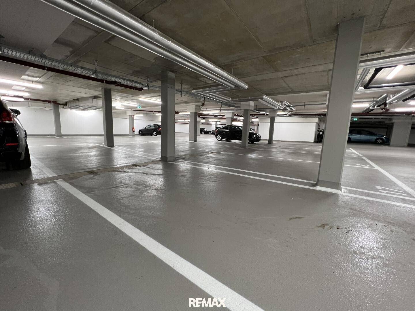 Weitläufige Tiefgarage mit mehreren geparkten Fahrzeugen und klar gekennzeichneten Stellplätzen.