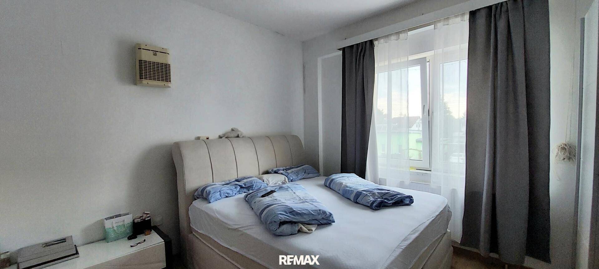 Schlafzimmer mit Doppelbett, Heizung und Fenster mit Vorhängen.