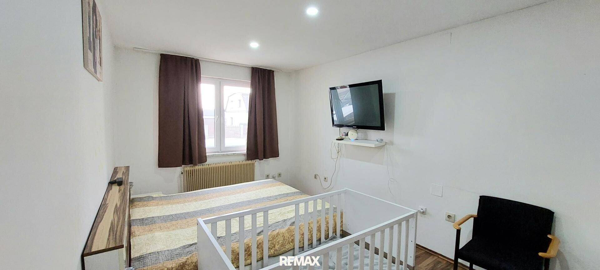 Schlafzimmer mit Doppelbett, Babybett und Fernseher an der Wand.