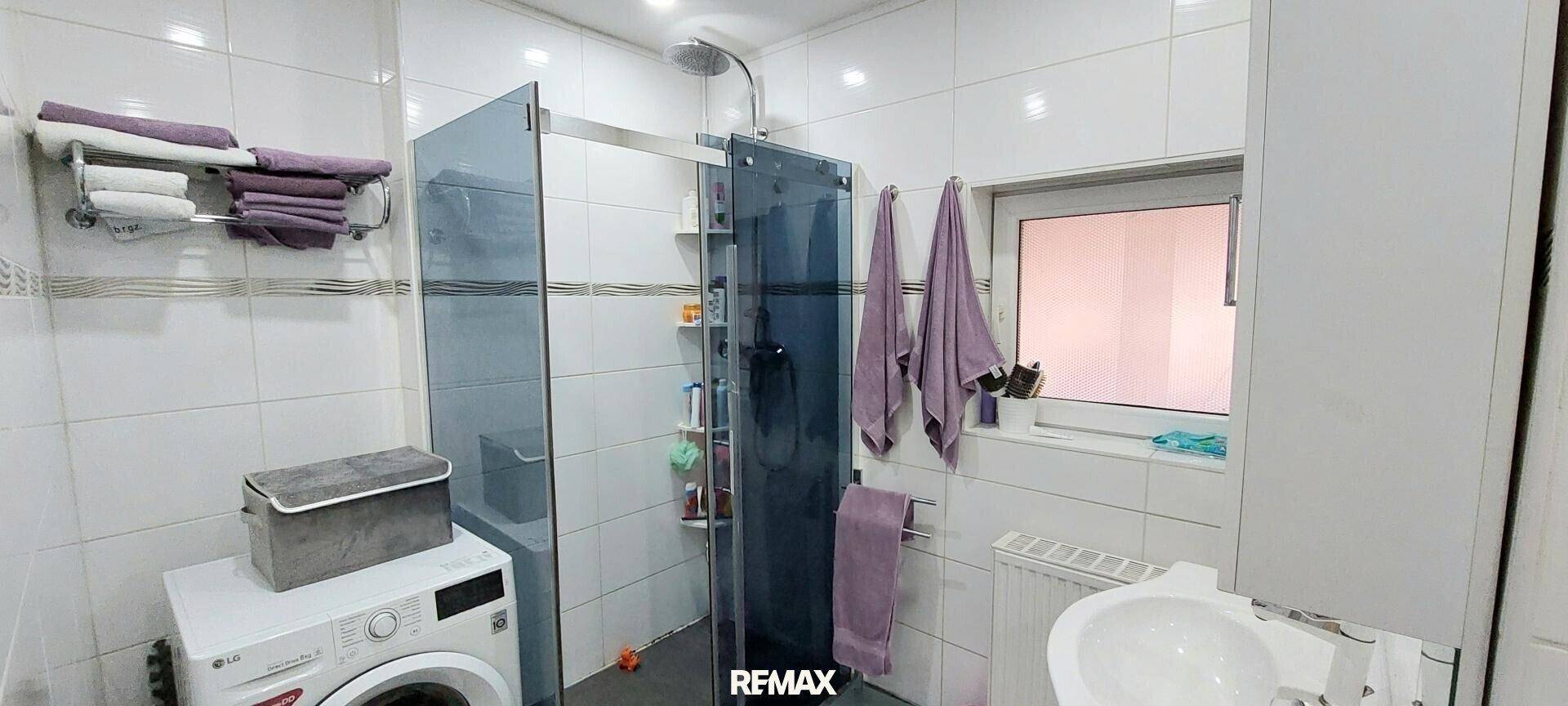 Modernes Badezimmer mit Duschkabine, Waschmaschine und hellen Fliesen.