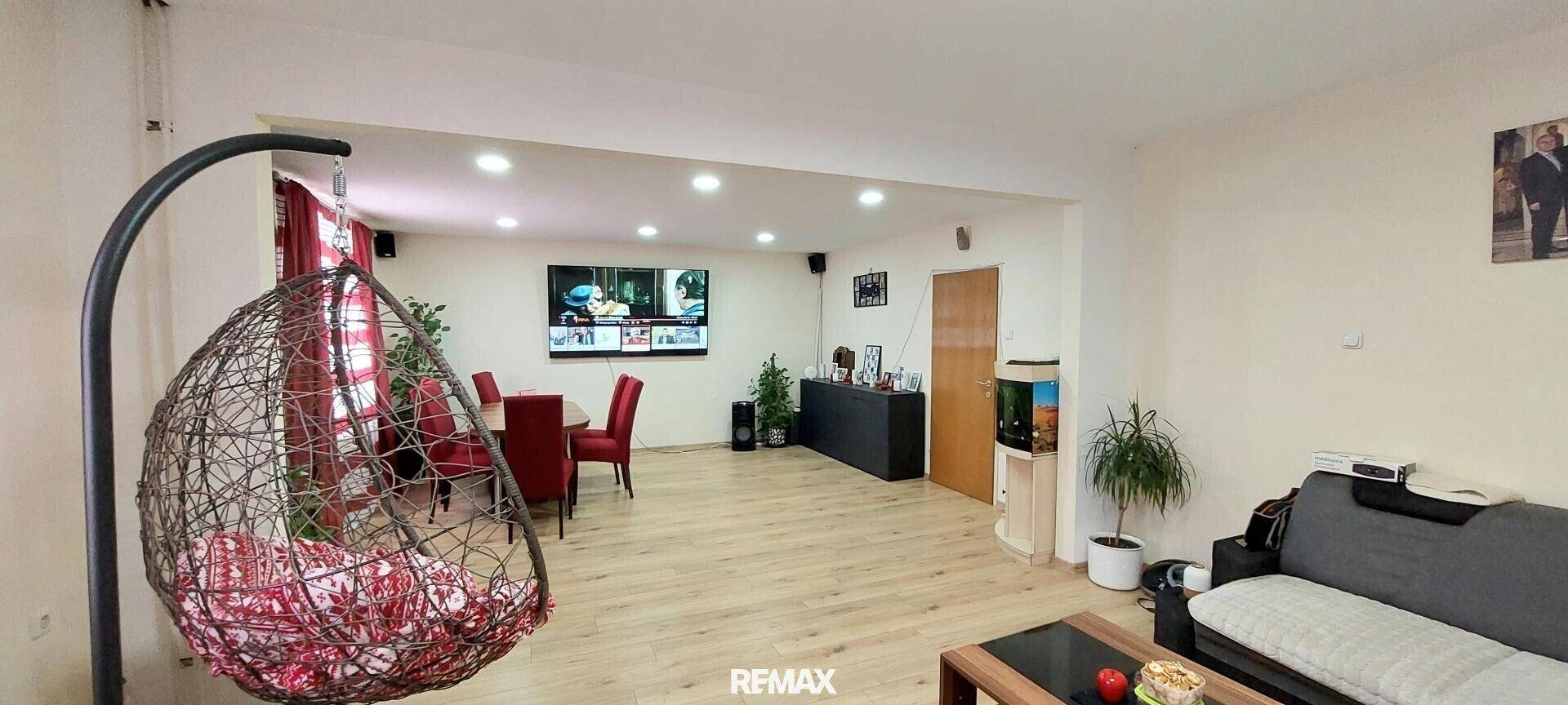Heller Wohn- und Essbereich mit Fernseher, Schaukelstuhl und Zugang zu weiteren Räumen.