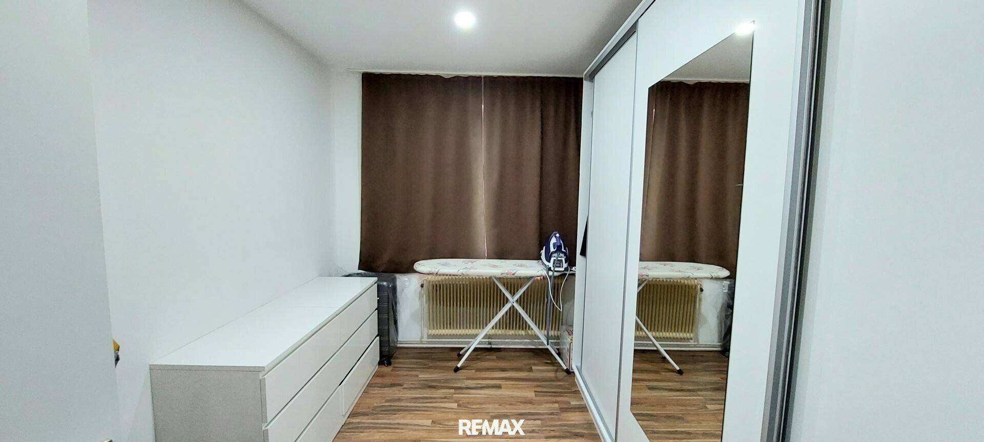 Raum mit Kleiderschrank, Bügelbrett und Fenster mit Vorhängen.