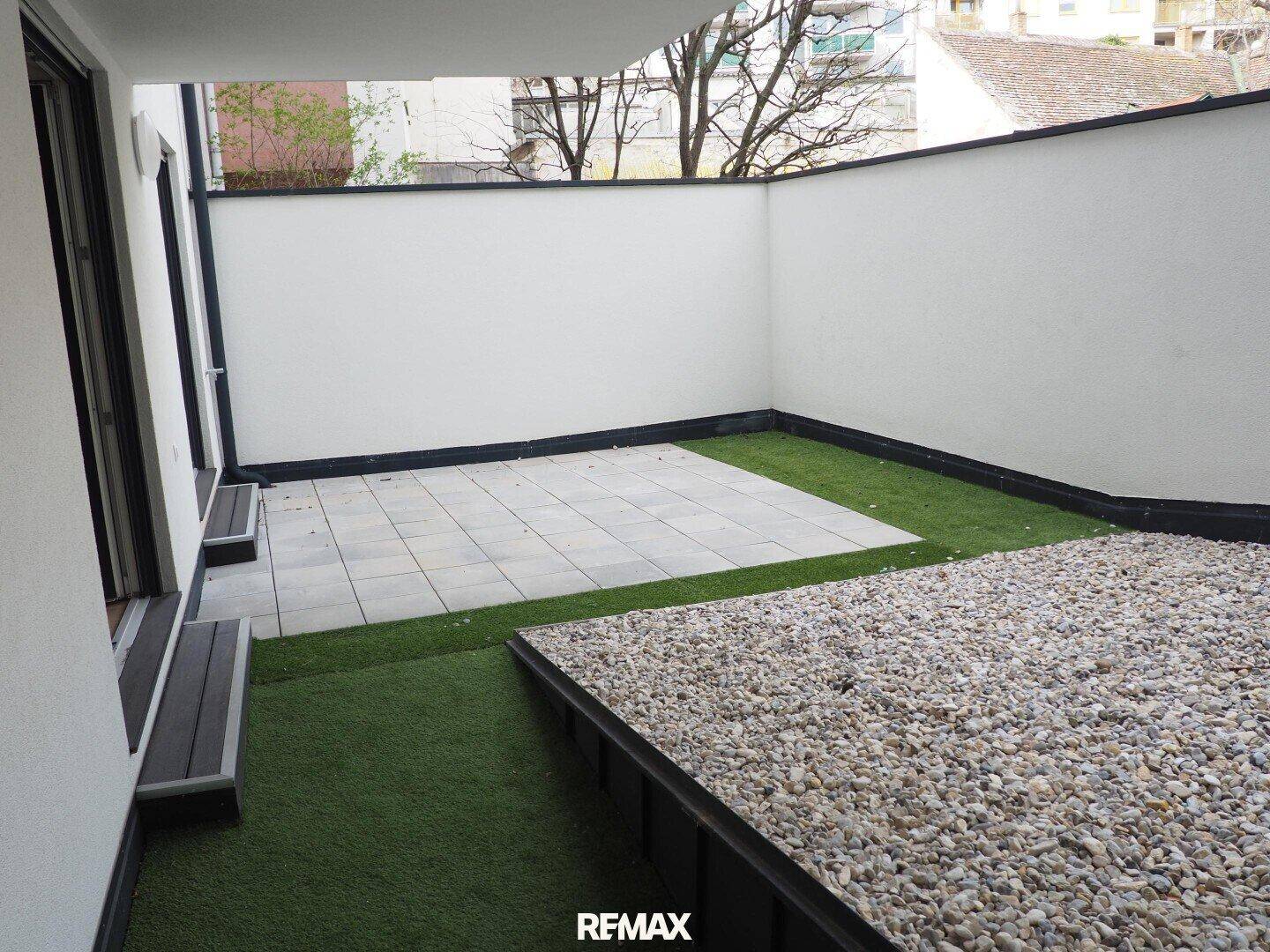Geschützte Terrasse mit hohen Wänden und einer Kombination aus Steinplatten und Kunstrasen.