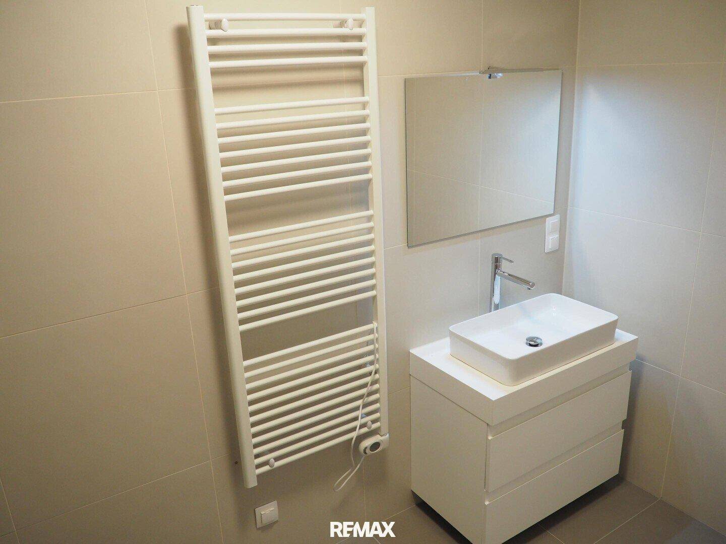Helles Badezimmer mit modernem Waschbecken, Spiegel und beheiztem Handtuchhalter.