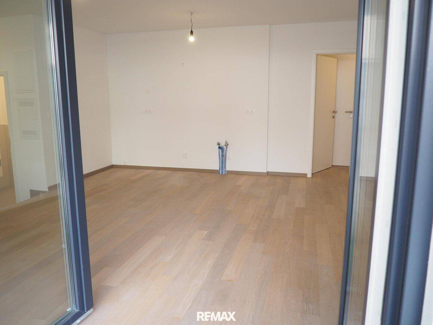 Leerer Raum mit Holzboden und sichtbaren Anschlüssen, bereit für die Kücheninstallation.
