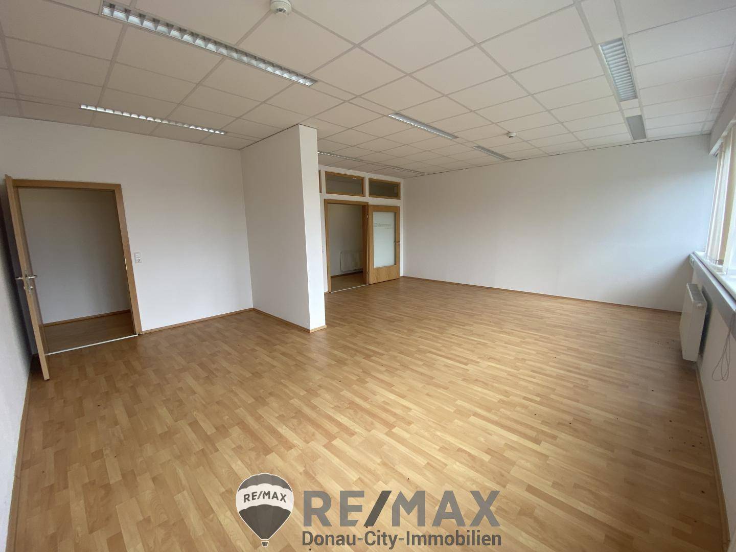 Geräumiges Büro mit hellem Holzboden und weißen Wänden, bereit für die Einrichtung.