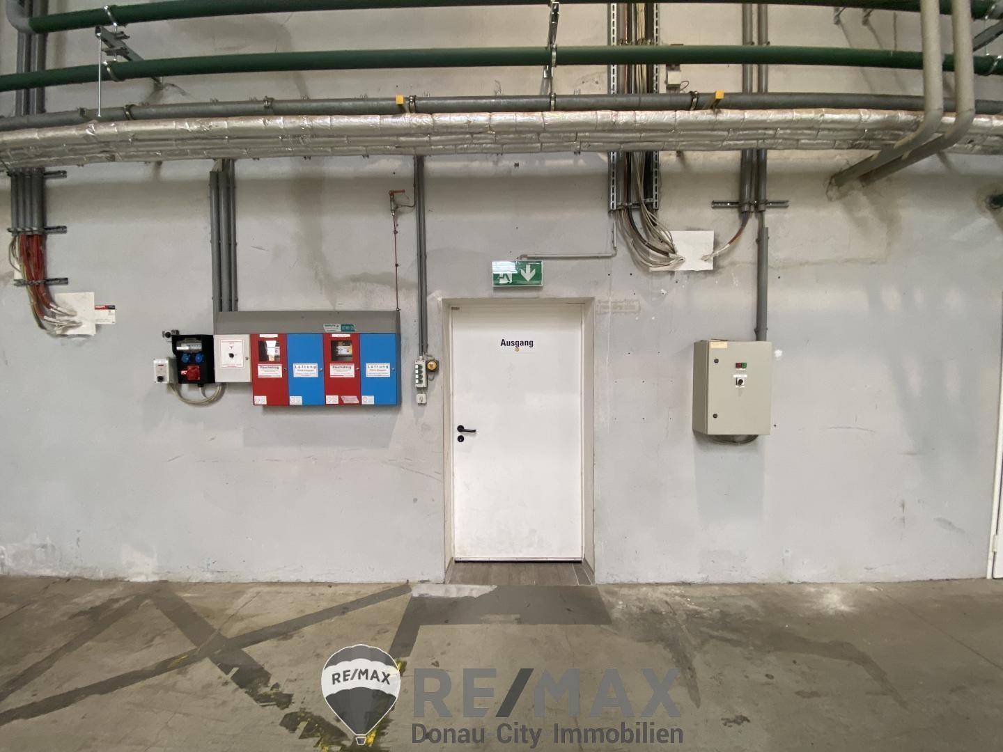 Flur mit einer Ausgangstür, umgeben von sichtbaren Rohrleitungen und elektrischen Installationen.