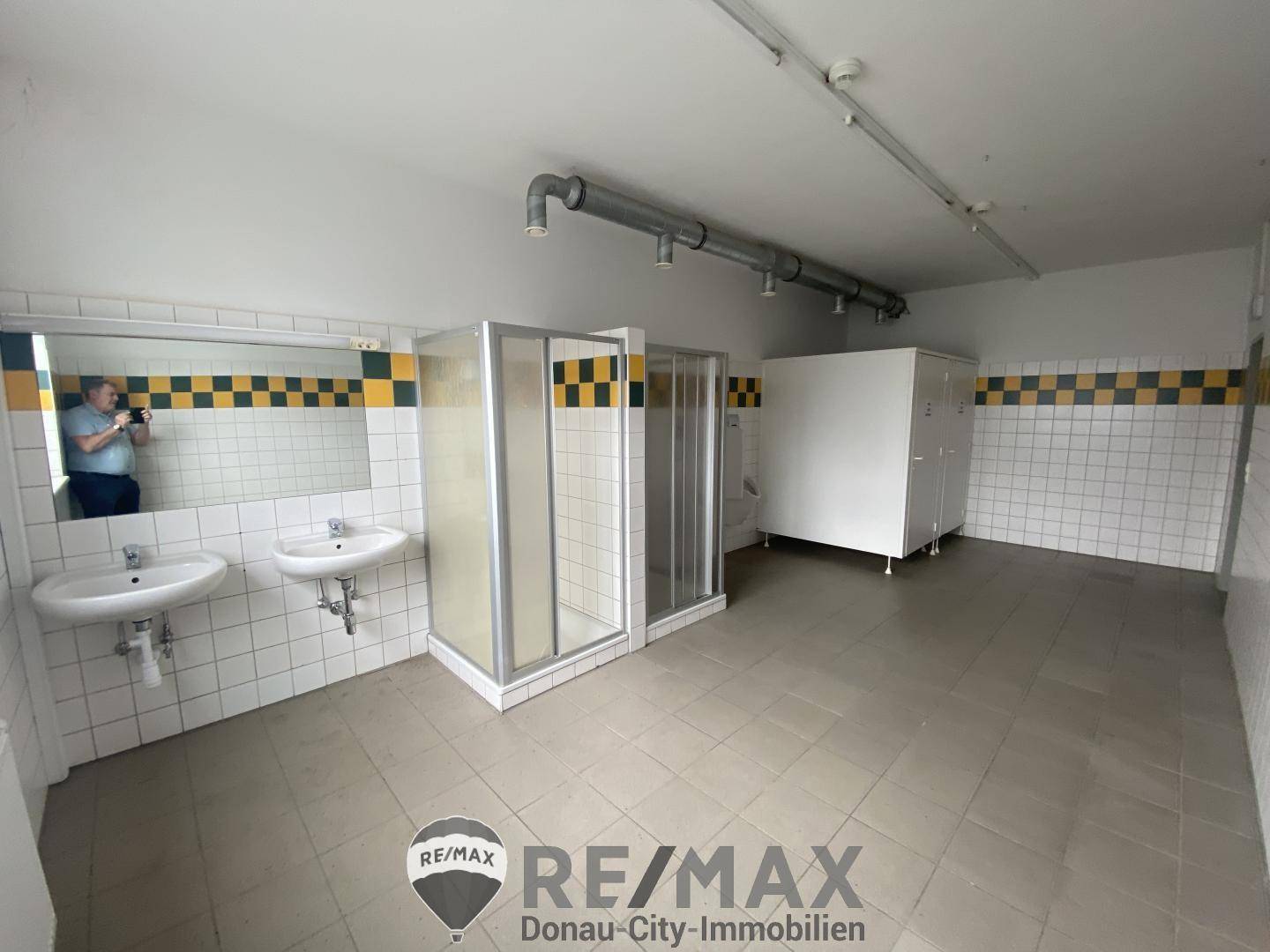 Umkleideraum mit zwei Duschkabinen, Waschbecken und gefliesten Wänden in Weiß und Gelb.