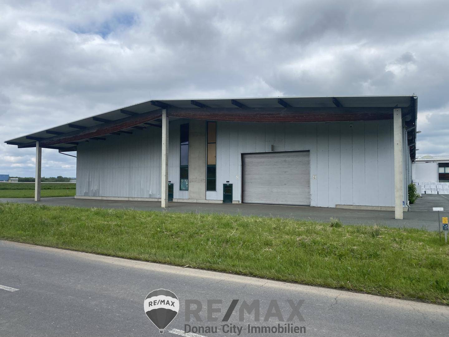 Modernes Industriegebäude mit großem Rolltor und überdachtem Eingangsbereich, umgeben von Grünflächen.