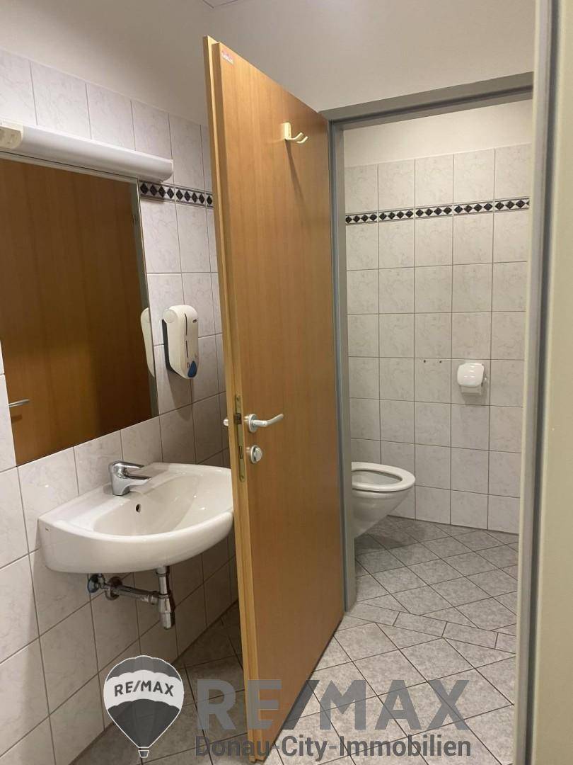 Saubere Toilette mit Waschbecken, Spiegel und weißen Fliesen, die einen funktionalen Eindruck macht.