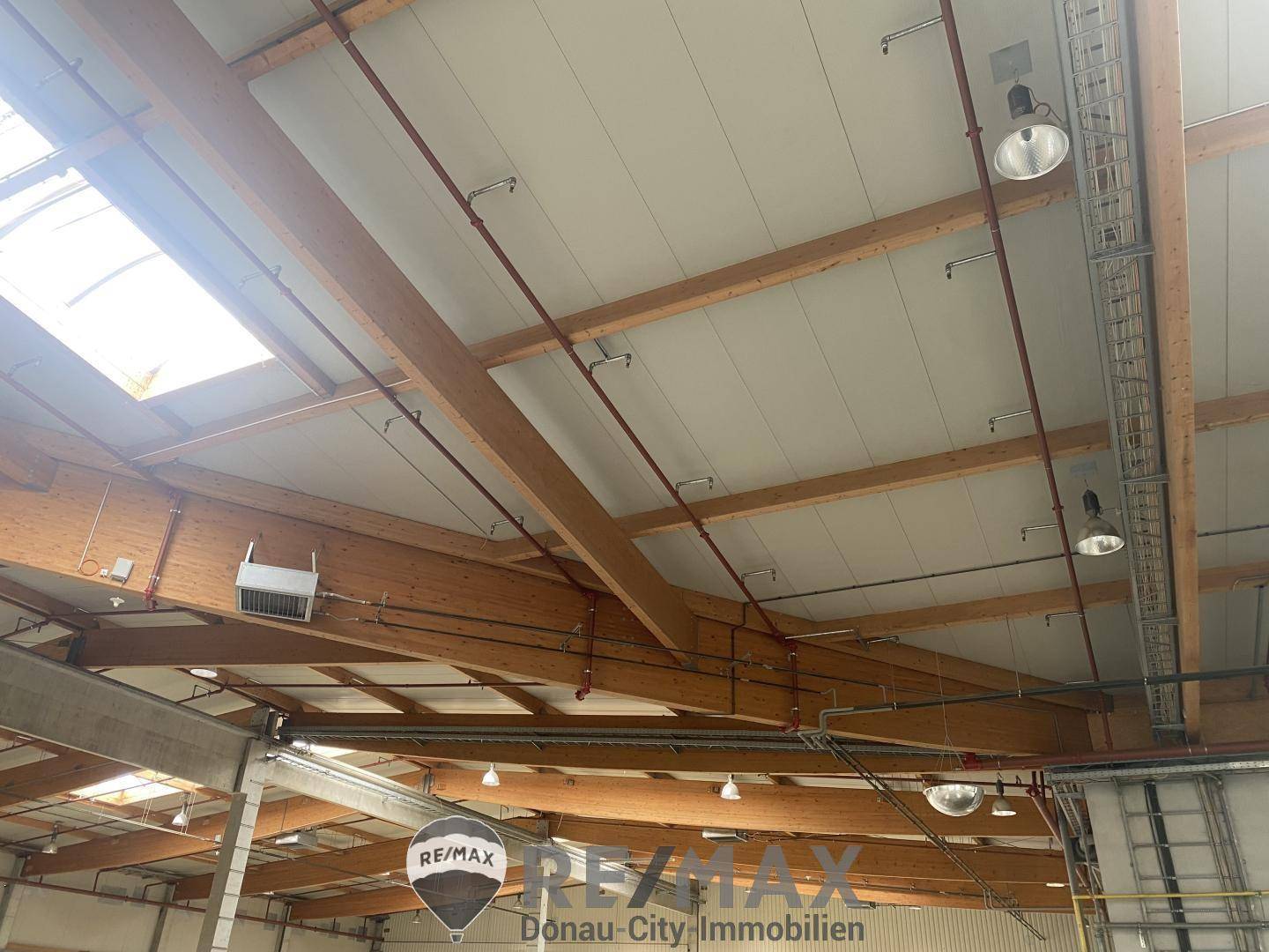 Hohe Decke einer Lagerhalle mit sichtbaren Holzbalken, Beleuchtung und Lüftungsrohren.